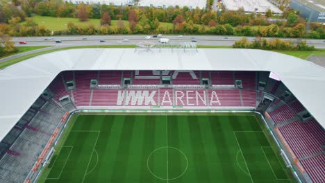Antenne-Fliegt-über-Das-Dach-Des-Leeren-Wwk-Arena-Stadions,-Heimat-Des-Fc-Augsburg,-Mit-Zweispuriger-B17-Im-Hintergrund