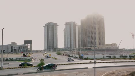 Pear-And-Reef-Towers-Seen-Through-Morning-Mist-With-Traffic-Going-Past-In-Karachi
