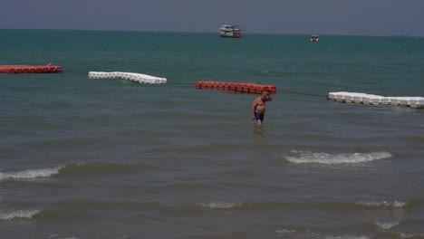 Un-Hombre-Nada-En-Las-Barreras-Flotantes-Rojas-Y-Blancas-Que-Brindan-Seguridad-A-Los-Nadadores-En-La-Playa-De-Pattaya,-Tailandia