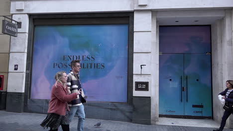 In-slow-motion-people-walk-past-an-empty-shop-space,-known-as-“dead-spaces”,-on-Argyll-Street-near-Oxford-Circus