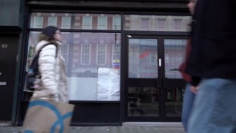 In-slow-motion-people-walk-past-an-empty-shop-space,-known-as-“dead-spaces”,-on-Tottenham-Court-Road