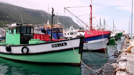 Row-of-colourful-wooden-boats-floating-in-Kalk-Bay-Cape-Town-harbour,-South-Africa