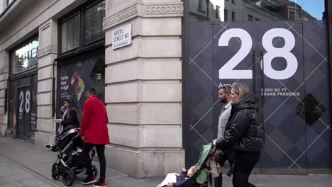 In-slow-motion-people-with-pushchairs-walk-past-an-empty-shop-space,-known-as-“dead-spaces”,-on-Argyll-Street-near-Oxford-Circus