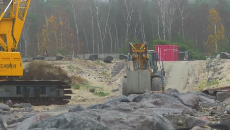 Construction-site-on-the-Baltic-sea-shore,-strengthening-the-Baltic-Sea-coastline,-building-protective-stone-pier,-heavy-duty-yellow-mover-delivering-large-concrete-block,-overcast-day