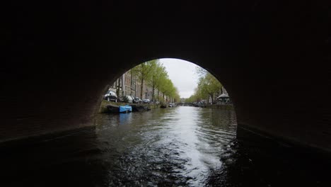 Amsterdam-view-from-a-boat-cruising-in-canal-under-bridge,-Cloudy-day,-Holland