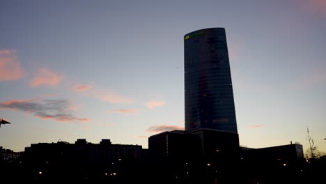 Iberdrola-Tower-electricity-consortium-silhouette-at-dusk-with-plane-passing-behind,-Wide-establishing-shot