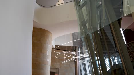 Glass-panes-and-string-light-fixture-inside-Guggenheim-Museum-by-architect-Frank-Gehry-seen-from-below,-Medium-shot