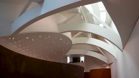 Support-arches-inside-Guggenheim-Museum-by-architect-Frank-Gehry-seen-from-the-floor-below-with-people-on-balcony,-Wide-stable-shot