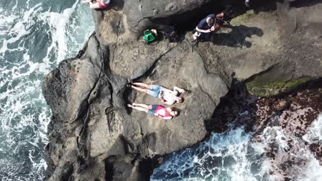 Das-Paar-Liegt-Auf-Der-Felsenhalbinsel,-Während-Die-Drohne-Schnell-Aufsteigt-Und-Das-Große-Bild-Von-Felsen-Und-Ozean-Macht