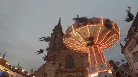 People-riding-the-chain-carousel-in-front-of-the-minster-at-the-autumn-fair-in-Basel,-Switzerland
