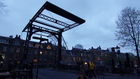 People-crossing-Aluminium-Bridge-in-old-city-Amsterdam,-Holland,-Evening