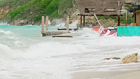 Local-wooden-fishing-boat-being-smashed-into-land-during-sudden-storm-with-rough-waves,-Caribbean