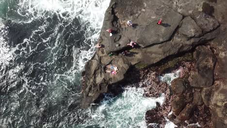 Das-Paar-Liegt-Auf-Der-Felsenhalbinsel,-Während-Die-Drohne-Aufsteigt-Und-Das-Große-Bild-Von-Felsen-Und-Ozean-Macht