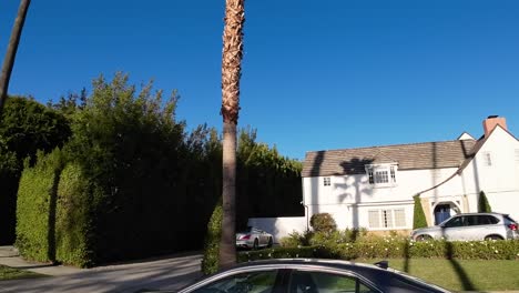 POV-Driving-Past-Affluent-Homes-In-Beverly-Hills,-Los-Angeles-On-Sunny-Clear-Day-With-Blue-Skies