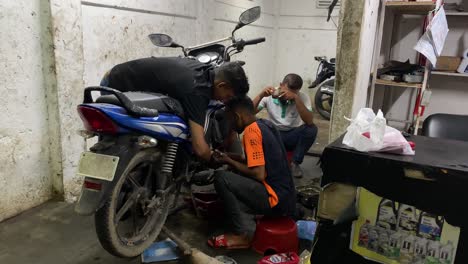 Group-of-mechanics-men-fixing-scooter-motorcycle-at-workshop-garage,-pan