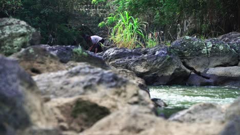 Asian-Man-searching-and-catching-fish-on-rocky-river-in-nature-during-sunny-day