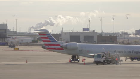Airport-American-Airlines-Aircraft-Parked-At-Airport-With-Smoke-Stacks-Seen-In-Background