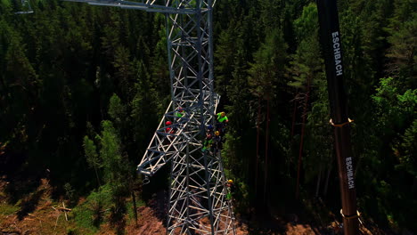 A-crew-climbs-up-and-electrical-transmission-tower-to-install-the-cables---tilt-down-aerial-view