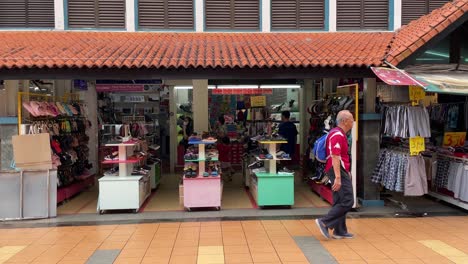 Man-with-a-backpack-walks-past-shops-at-Toa-Payoh-Central,-Singapore