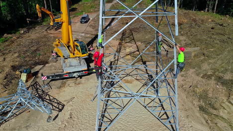 Crane-and-crew-erecting-an-electrical-transmission-pylon-tower-near-Jurmala,-Latvia---aerial-view