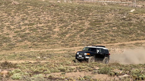 View-Of-4x4-SUV-Driving-Along-Dirt-Road-And-Pulling-Up-To-Park-In-Desert-Mountain-Landscape
