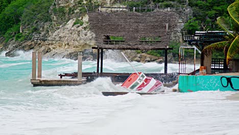 Local-wooden-fishing-boat-being-smashed-to-pieces-on-land-during-sudden-storm-with-rough-waves,-Caribbean