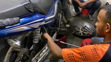 High-angle-closeup-of-mechanic-man-fixing-motorcycle,-handheld,-interior