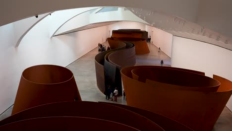 The-Matter-of-Time-abstract-metal-sculpture-by-Richard-Serra-inside-the-Guggenheim-Museum-with-people-walking-around-it,-Wide-stable-shot