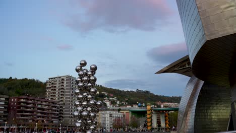 Tall-Tree-and-the-Eye-sculpture-by-Anish-Kapoor-outside-Guggenheim-Museum-with-residential-buildings-behind,-Wide-shot