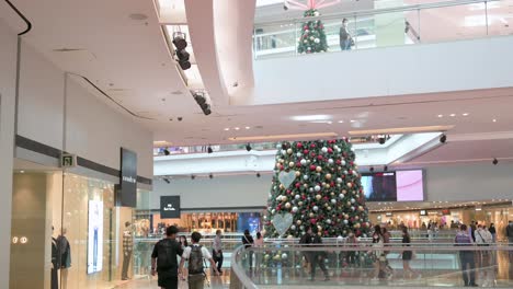 Chinesische-Käufer-Gehen-Durch-Ein-Einkaufszentrum,-Während-Im-Hintergrund-Eine-Großformatige-Weihnachtsbauminstallation-In-Hong-Kong-Zu-Sehen-Ist