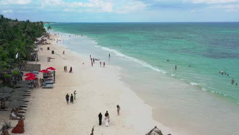tourists-on-tropical-white-sand-beach-in-Tulum's-Hotel-Zone-on-sunny-summer-day,-aerial