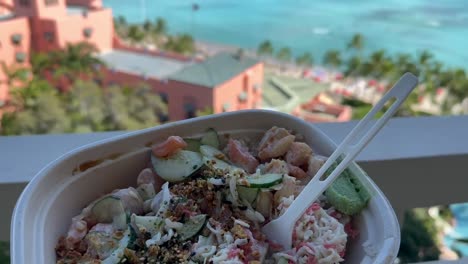 Persona-Sosteniendo-Un-Delicioso-Tazón-De-Poke-Hawaiano-Desde-El-Balcón-Del-Hotel-Con-Vista-A-La-Playa-De-Waikiki