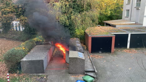 Flames-burst-out-of-a-waste-container,-domestic-trash-bin-in-a-backyard,-black-smoke