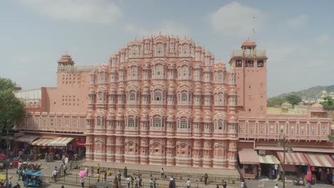 Hawa-Mahal-Soleado-Tiro-Amplio-Con-Tráfico-En-Primer-Plano-Y-Vistas-De-La-Hermosa-Atracción-Turística-Popular-En-Jaipur,-Rajasthan,-India,-Cielo-Despejado-Día-Soleado
