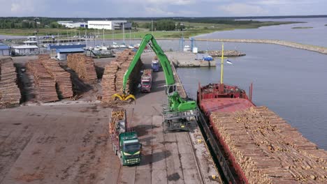 Crane-loads-timber-logs-from-truck-onto-cargo-ship-in-port-full-of-log-piles,-wide-shot,-static