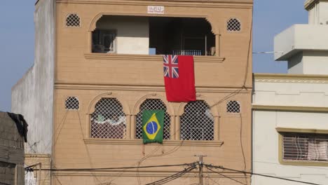 Red-Ensign-and-Brazil-Flag-Hanging-Over-Balcony-In-Malir,-Pakistan