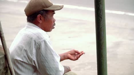 Slow-motion-video---close-up-shot-of-poor-man-is-sitting-on-the-side-of-road-and-smoking-cigarette,-close-up-side-view