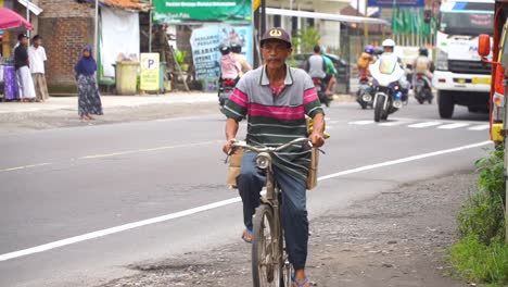 Video-En-Cámara-Lenta---El-Anciano-Está-Montando-Una-Bicicleta-Vieja-Al-Lado-De-La-Carretera,-Indonesia