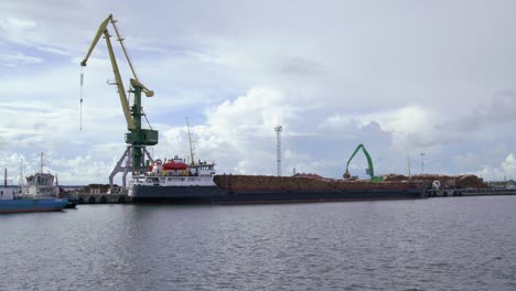 Cargo-ship-at-timber-port-full-of-logs-loaded-onto-ship-by-crane,-static,-ultra-wide-shot