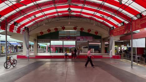 People-rest-in-the-common-area,-and-a-man-walks-towards-the-hawker-centre-in-Chong-Pang-City-neighbourhood,-Singapore
