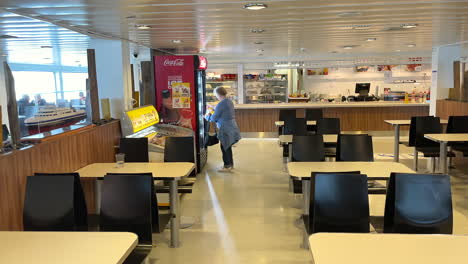 Tourist-taking-out-a-cold-drink-inside-a-Norwegian-ferry-in-the-cafeteria,-panning-shot