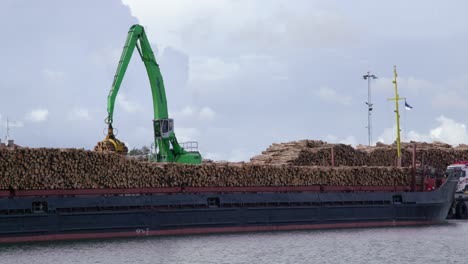 Crane-moves-from-right-to-left-to-load-timber-logs-onto-cargo-ship,-static,-wide-shot