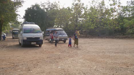Small-Asian-family-walking-on-dirty-rural-road-while-old-buses-pass-by