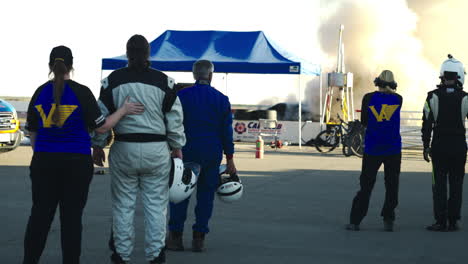 People-watching-race-car-burning-after-big-explosion