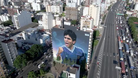 Birds-eye-view-flyover-highway-capturing-largest-mural-of-Maradona-in-Buenos-Aires-to-commemorate-soccer-legend-on-his-anniversary-of-death,-with-heavy-traffics-on-one-side-of-autopista-25-de-mayo
