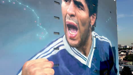 World-cups-superstar-player,-hand-of-god-Diego-Maradona-wall-mural-in-neighborhood-of-Constitución-by-Martin-Ron-dedicated-to-the-legend-on-his-second-anniversary-of-death,-aerial-elevation-down-shot