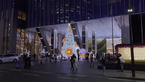 Chinesen,-Die-Nachts-Am-Hoteleingang-Mit-Einer-Riesigen-Weihnachtsbauminstallation-Vorbeigehen