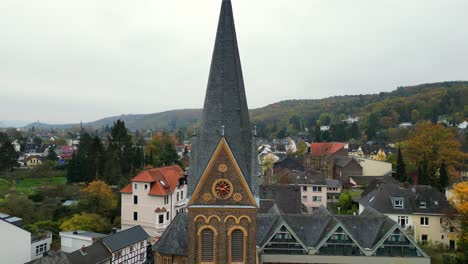 Pull-back-drone-shot-of-church-in-Dottendorf,-Germany-showing-a-gold-clock-and-the-neighbourhood-in-the-background
