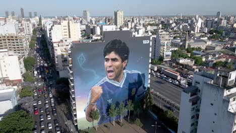 Giant-Maradona-emerges-in-Argentina,-days-before-World-Cup,-mural-of-late-soccer-legend-unveiled-in-the-middle-of-concrete-jungle-in-the-heart-of-Buenos-Aires,-aerial-forward-flying-close-up-shot