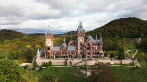 Push-out-shot-of-the-front-of-the-Drachenburg-Castle-situated-in-the-Drachenfels,-Königswinter,-Germany-with-a-beautiful-autumn-sun-and-coloured-leaves